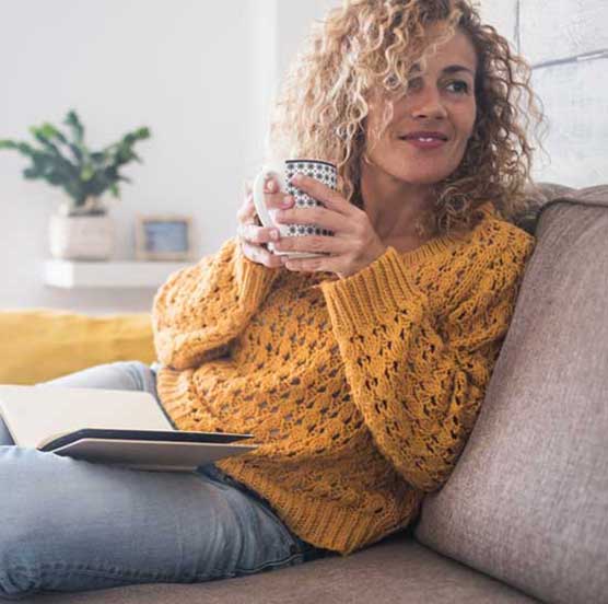 Frau sitzt auf einem Sofa mit einem heißen Getränk